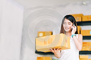 Small business owner, Asian woman hold package box, using mobile phone call receiving purchase order, working at home office