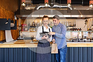 Small business owner couple in little family restaurant looking at tablet for online orders