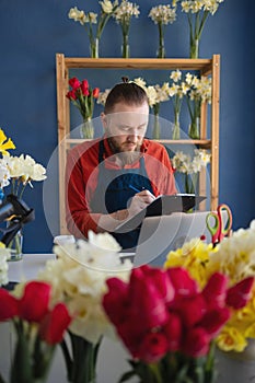 Small business owner florist working with laptop and clipboard in his flower shop. concept of own business