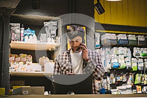 Small business owner on phone and computer in store. Sport shop worker making call with cell phone. Salesman working and talking