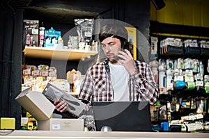 Small business owner on phone and computer in store. Sport shop worker making call with cell phone. Salesman working and talking