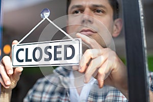 Small Business Owner With Serious Expression Putting Up Closed Sign During Recession Or Health Pandemic