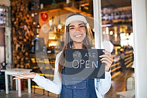 Small business owner smiling while holding the sign for the reopening of the place after the quarantine due to covid-19. Woman