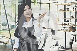 small business owner standing at coffee shop. female barista wearing apron smiling at cafe. food service, restaurant concept.