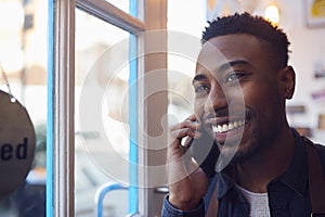 Small Business Owner Standing By Shop Door Making Call On Mobile Phone