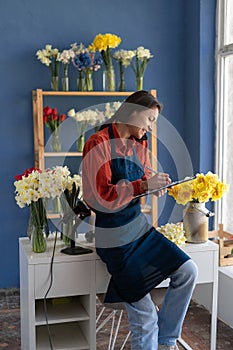 Small business owner woman flower shop owner working at workplace calling client and writing orders on clipboard