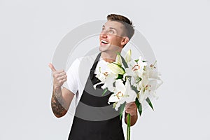 Small business, retail and employees concept. Handsome florist, salesman in flower shop pointing upper left corner