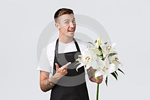 Small business, retail and employees concept. Handsome salesman in black apron, pointing finger at beautiful flowers