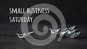 Small business Saturday concept. Many Origami ships from US dollars on dark background with text Small business Saturday