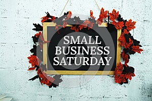 Small Business Saturday text message on Blackboard decoration with maple leaves hanging on a concrete wall background