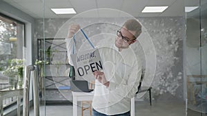 Small business success, attractive young entrepreneur rejoices at the opening of the store and stands with a sign open