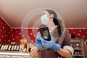 Small businesses during the pandemic. Portrait of a female worker in medical gloves and a mask using a cellphone. Bottom view.