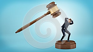 A small businessman tries to avoid a giant gavel strike while standing on a sound block. photo