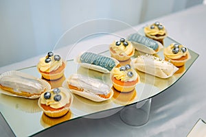 Small cakes, cupcakes, eclairs, close-up. Sweets on unusual plate, interesting presentation. Restaurant service, anniversary