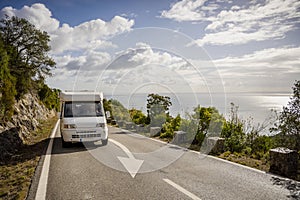 Small camper van driving on scenic road with sea views in Arrabida Natural Park, Portugal