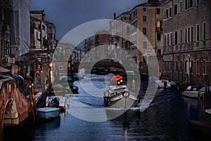 small canal with little boat with people with red umbrella and old houses in row on dusk in rainy day in Venice, Italy