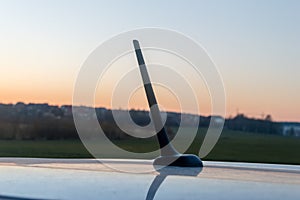 Small car antenna on the roof. Radio antenna with sunset background