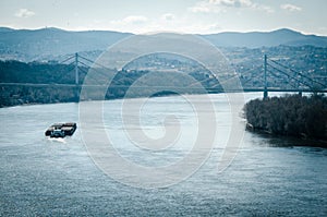 Small cargo ship sailing on the Danube river near bridge in Novi Sad, Serbia.