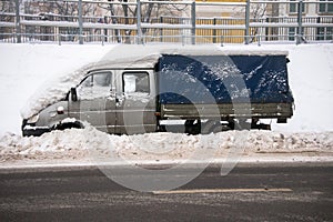 A small cargo tent van, covered with thick layer of snow and mud, on the roadway.