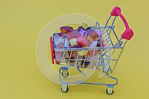 A small cart from a supermarket on a yellow background, filled with colorful candies and marmalade. Idea - shopping, home delivery