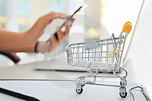 Small cart on table of woman using mobile phone and laptop. Internet shopping concept