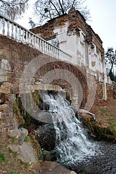 A small cascading waterfall near the ruins of an old house and a fence in an ancient park
