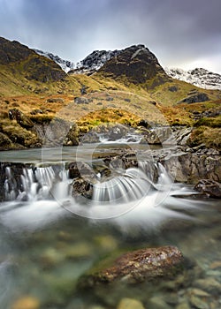 Small Cascading Waterfall Stream At Deepdale Beck In The Lake District National Park With Snow On Mountain Peaks.