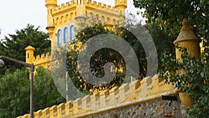 Small castle tower painted in yellow behind stone roofed wall, vertical panorama