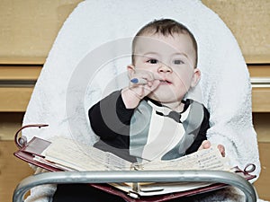 Small caucasian baby boy sitting in chear with notepad