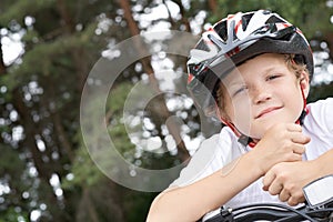 Small Caucasian boy cyclist in protective helmet put his head on the handlebar of the bike posing for the camera. a Boy