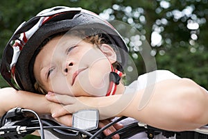 Small Caucasian boy cyclist in protective helmet put his head on the handlebar of the bike posing for the camera. a Boy