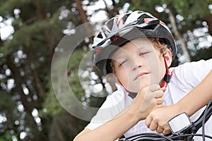 Small Caucasian boy cyclist in protective helmet put his head on the handlebar of the bike posing for the camera. a Boy