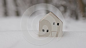 Small ceramic Christmas house outdoors in winter. A snow covered bird house in winter forest. Winter background