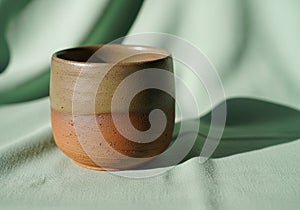 A small ceramic cup on a light green fabric backdrop. The cup