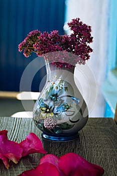 a small ceramic vase with purple flowers and pink patels of roses