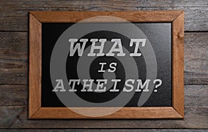 Small chalkboard with phrase What Is Atheism? on wooden background