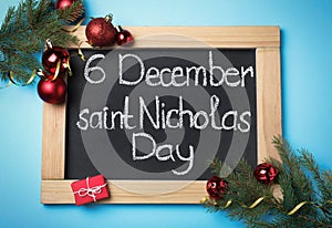 Small chalkboard with text 6 December Saint Nicholas Day and festive decor on light blue background, flat lay