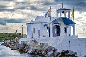 Small chapel with white roofs on cliff over sea and small bay under a dramatic sky on a Greek island