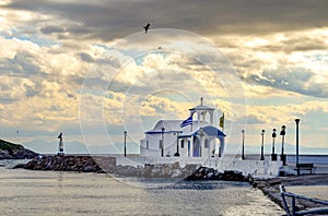 Small chapel with white roofs on cliff over sea and small bay under a dramatic sky on a Greek island