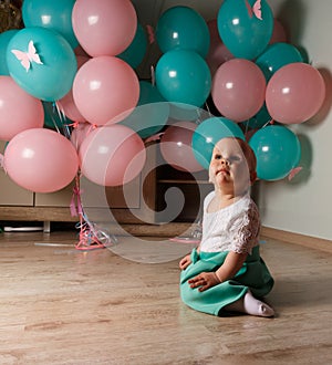 A small, charming child, a girl, celebrates her first birthday, sitting next to her with balloons. Children`s Party Organization.