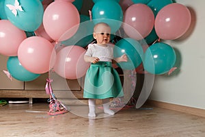 A small, charming child, a girl, celebrates her first birthday, sitting next to her with balloons. Children`s Party Organization.