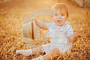 Small charming chubby little boy in a white suit holding a hat ,