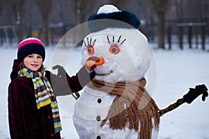 A small cheerful girl holds a big carrot, the nose of a big snowman