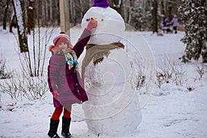 A small cheerful girl holds a big carrot, the nose of a big snowman