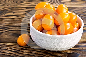 Small cherry tomatoes in a white bowl on a wooden background. The concept of consumption of locally produced goods.