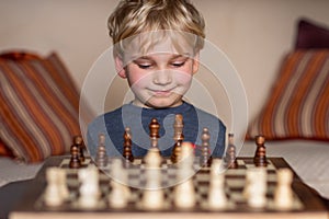Small child 5 years old playing a game of chess on large chess board. Chess board on table in front of the boy thinking of next