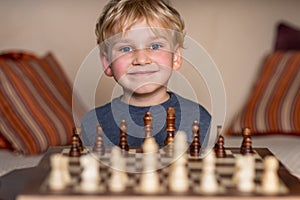 Small child 5 years old playing a game of chess on large chess board. Chess board on table in front of the boy thinking of next