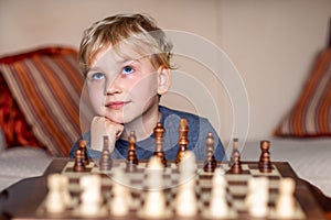 Small child 5 years old playing a game of chess on large chess board. Chess board on table in front of the boy thinking of next