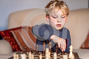 Small child 5 years old playing a game of chess on large chess board. Chess board on table in front of the boy thinking of next