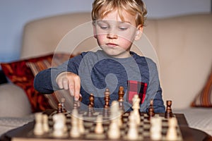 Small child 5 years old playing a game of chess on large chess board. Chess board on table in front of the boy thinking of next
